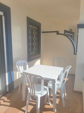 A patio with a white table and chairs, a decorative window, and a wall-mounted shelf. - Family Apartment in Punta del Moral (Isla Canela) (Ayamonte)