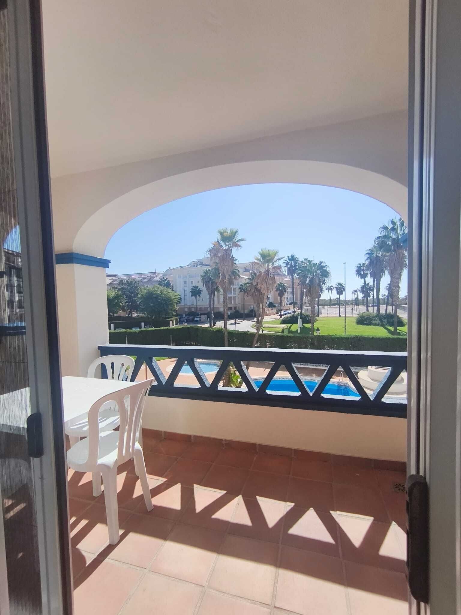 A balcony with a view of a pool, palm trees, and buildings in the distance.