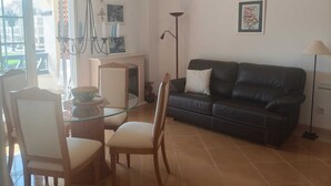 Ein Wohnzimmer mit einer schwarzen Ledersofa, einem Glastisch mit Stühlen, einem Kamin und einer Stehlampe.