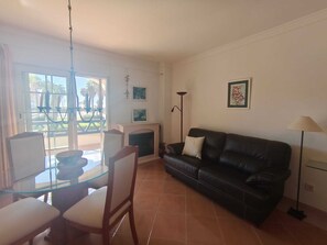 A living room with a glass dining table, a black leather sofa, a fireplace, and a floor lamp. - Family Apartment in Punta del Moral (Isla Canela) (Ayamonte)