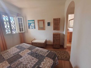A bedroom with a bed, a small bench, a wooden cabinet, and a window with a view. - Family Apartment in Punta del Moral (Isla Canela) (Ayamonte)
