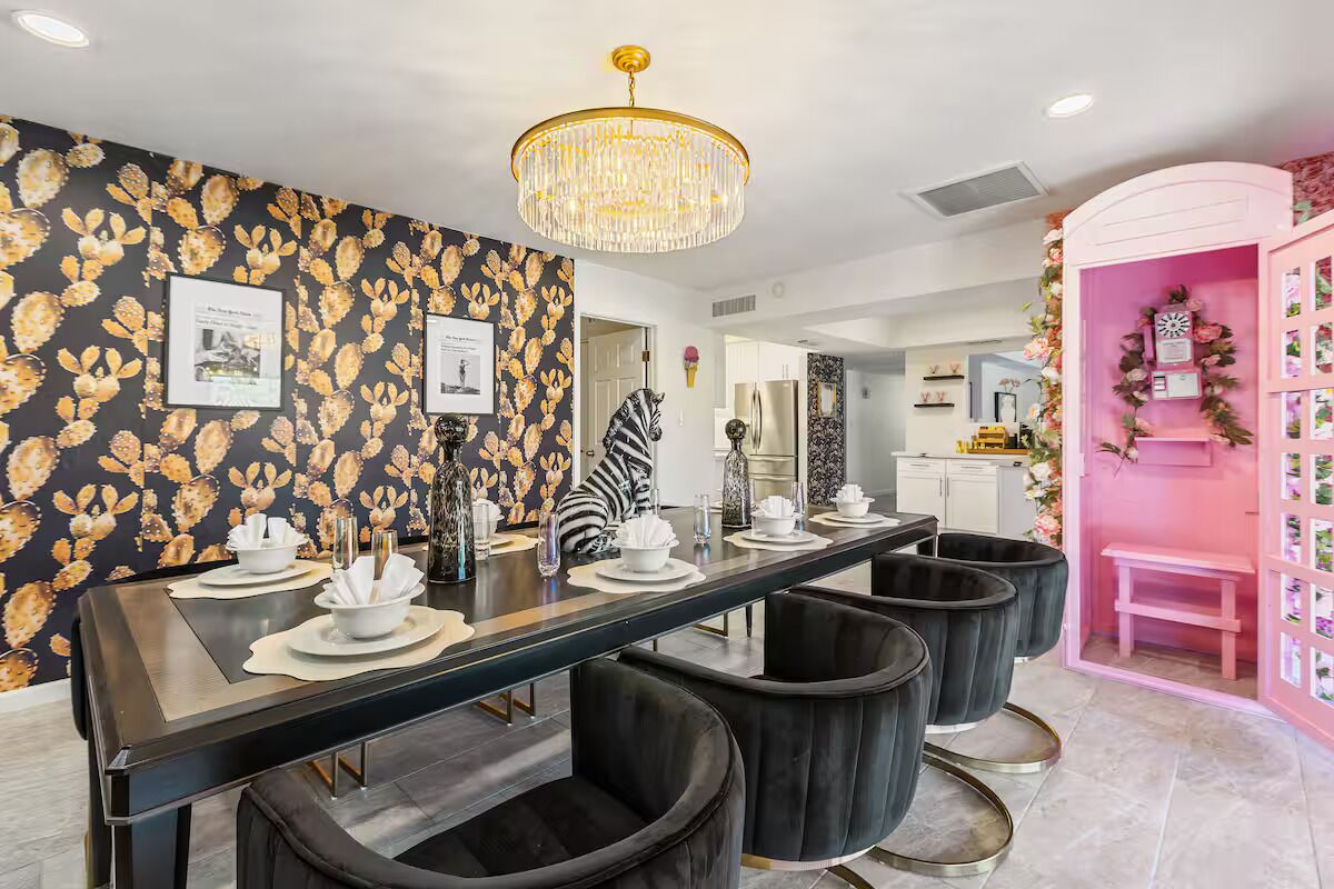 A dining area with a long table set for four, black chairs, and a chandelier.