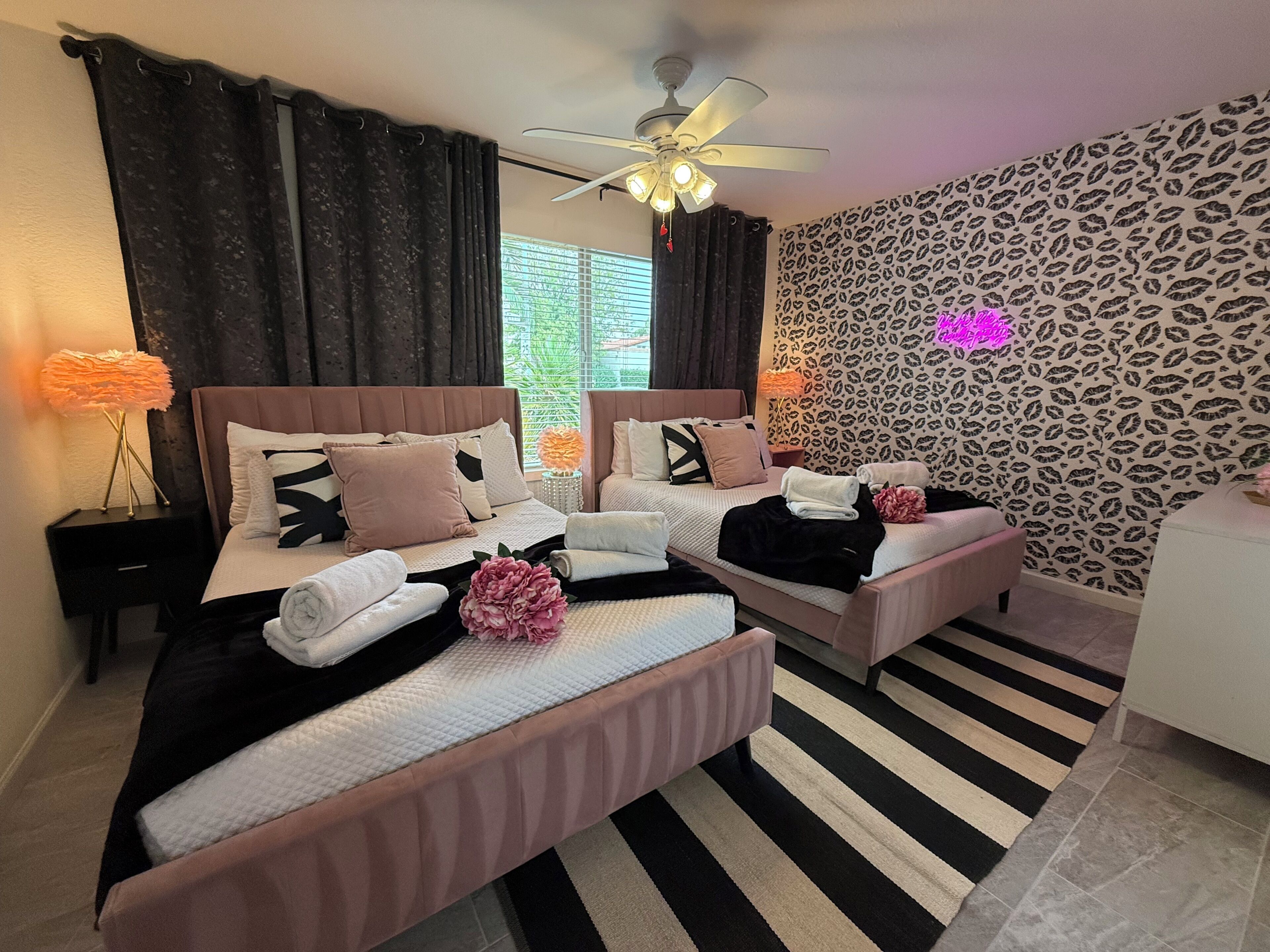 Une chambre d’hôtel avec un grand lit, deux petits lits, un ventilateur de plafond et un tapis à rayures.