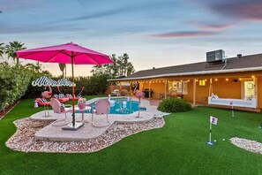 Un jardin avec une piscine, un espace salon extérieur et une terrasse couverte.