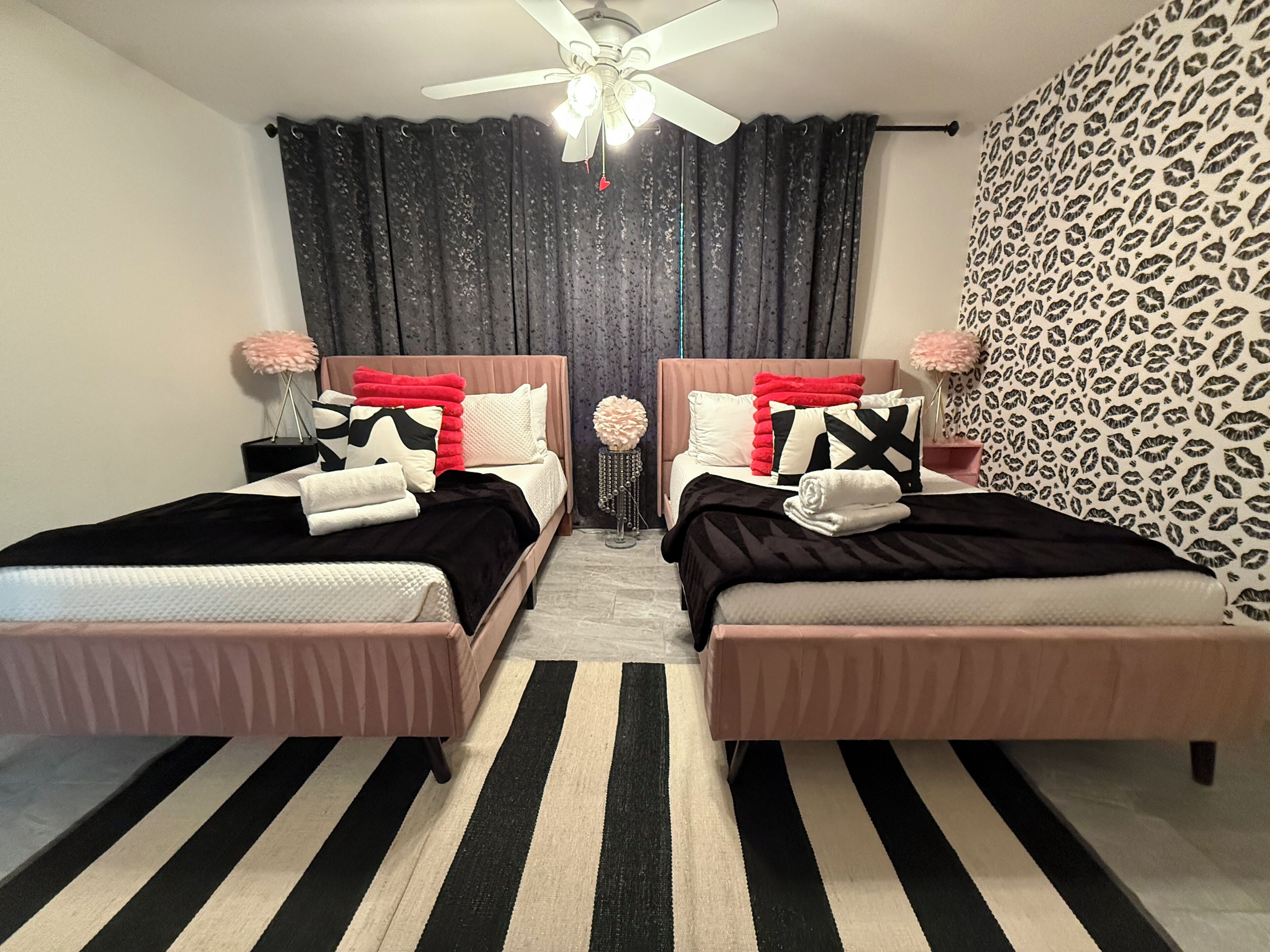Een kamer met twee bedden, een plafondventilator en een gestreept vloerkleed.