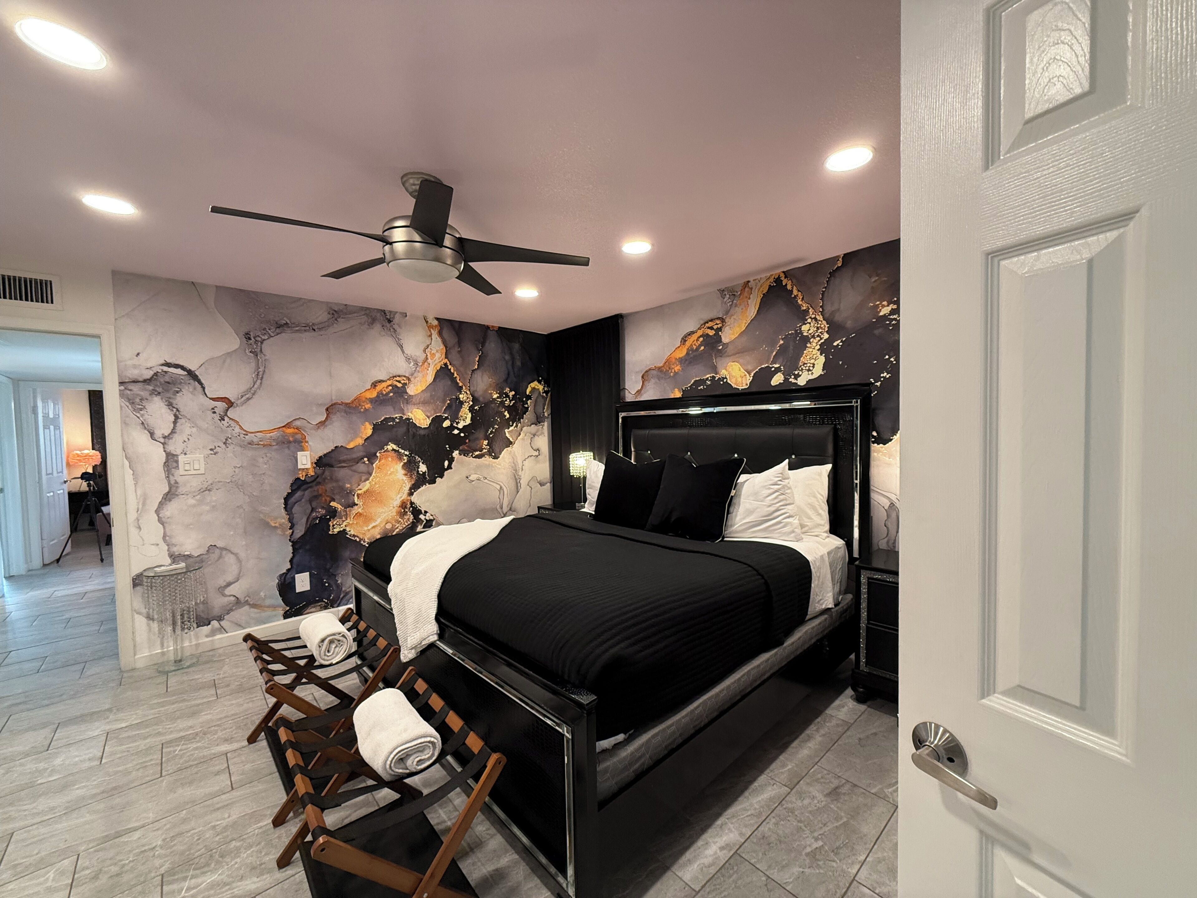 A modern bedroom with a bed, a ceiling fan, and a marble wall.