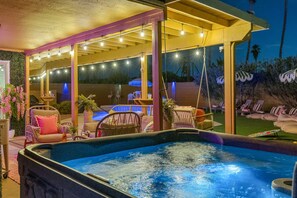 Un espace avec un bain à remous, agrémenté d’un coin salon couvert, de guirlandes lumineuses et de mobilier d’extérieur.