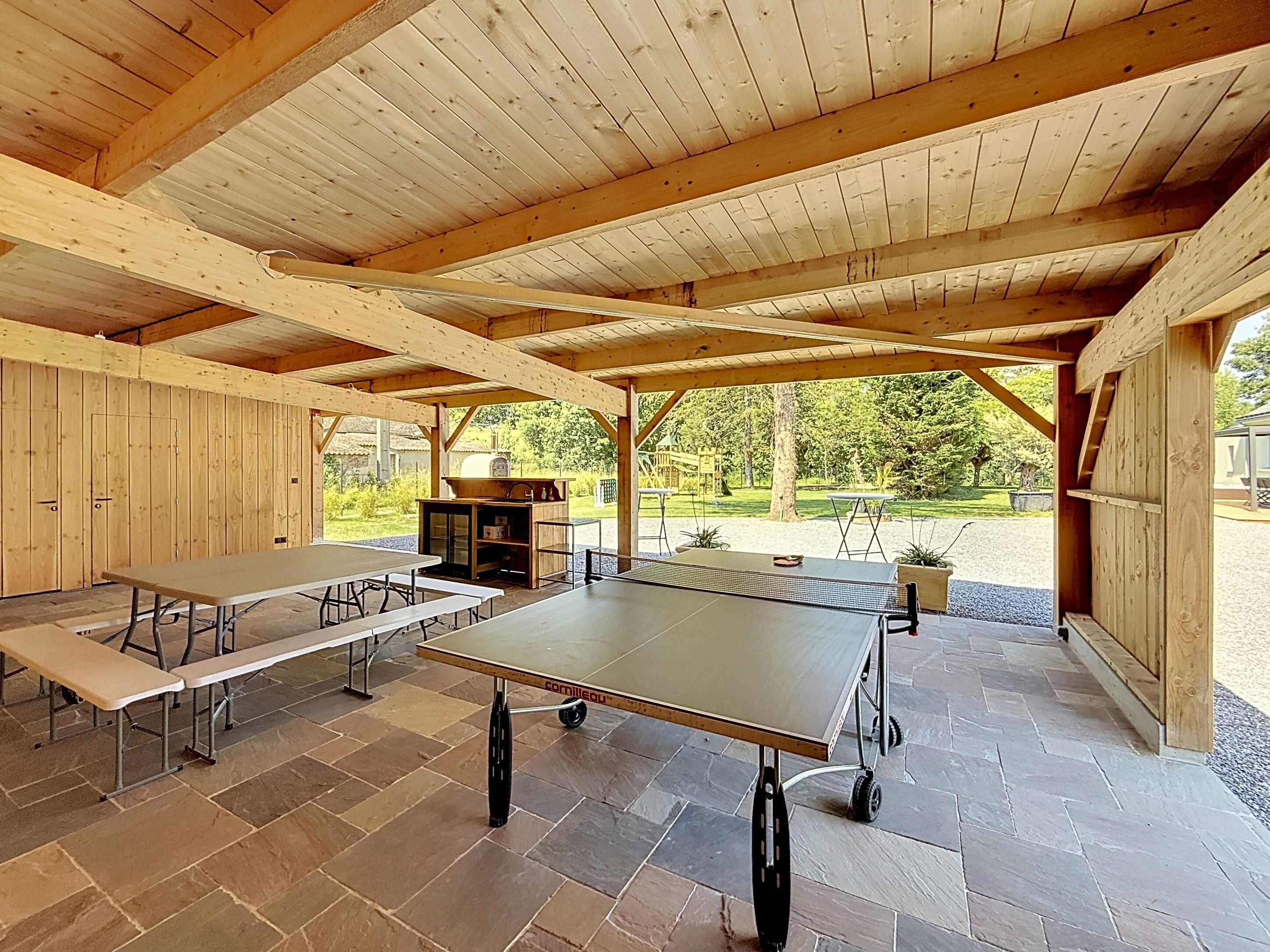Un espace extérieur abrité avec des tables de pique-nique et un barbecue.