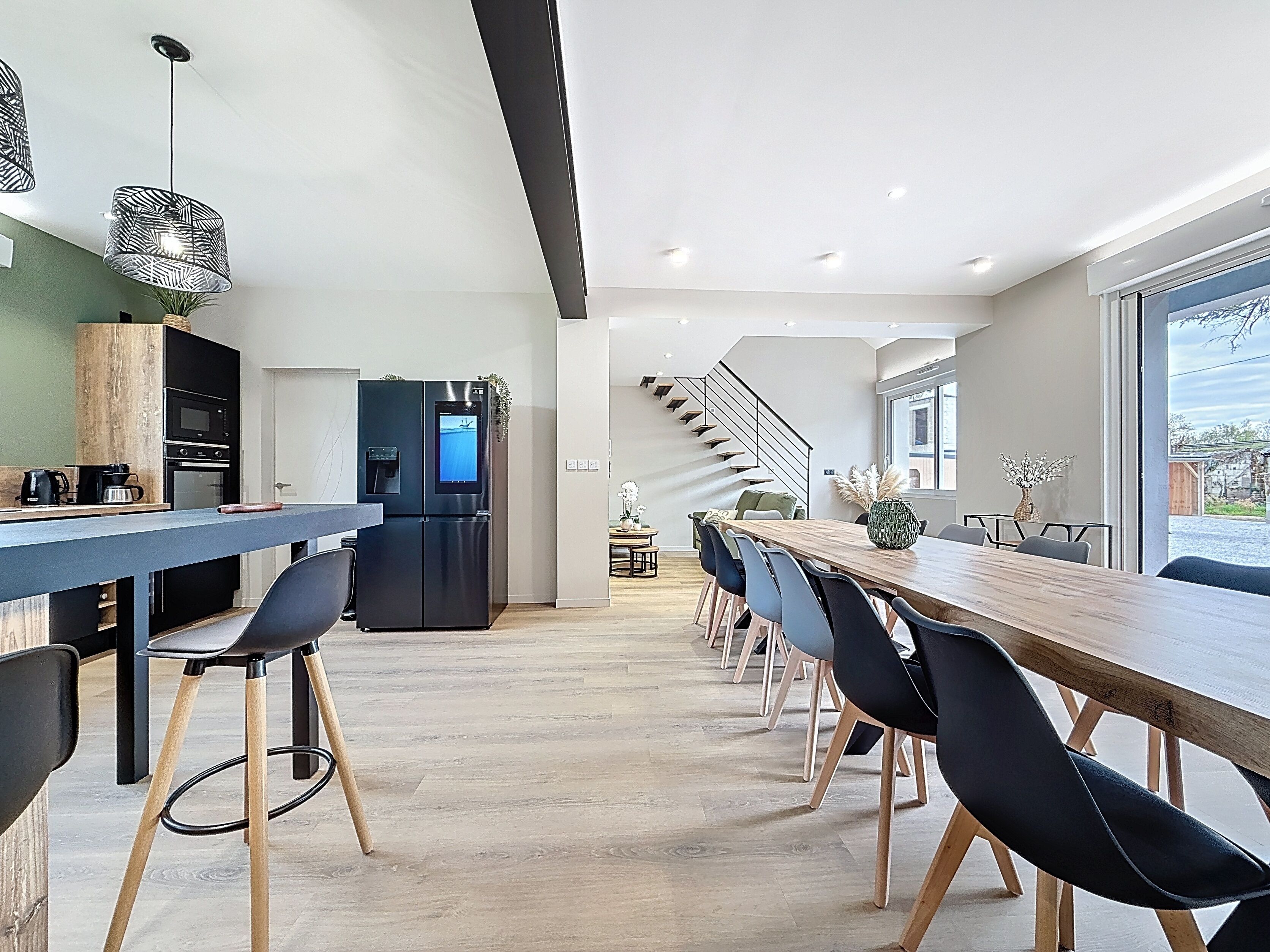 Eine moderne Küche mit eingebautem Ofen und Mikrowelle, ein Essbereich mit einem langen Holztisch und Stühlen sowie eine Treppe, die in eine obere Etage führt.