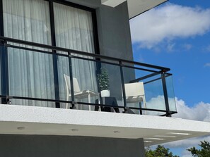 Ein Balkon mit Glastrennwand, einem Blumentopf und Blick zum Himmel.