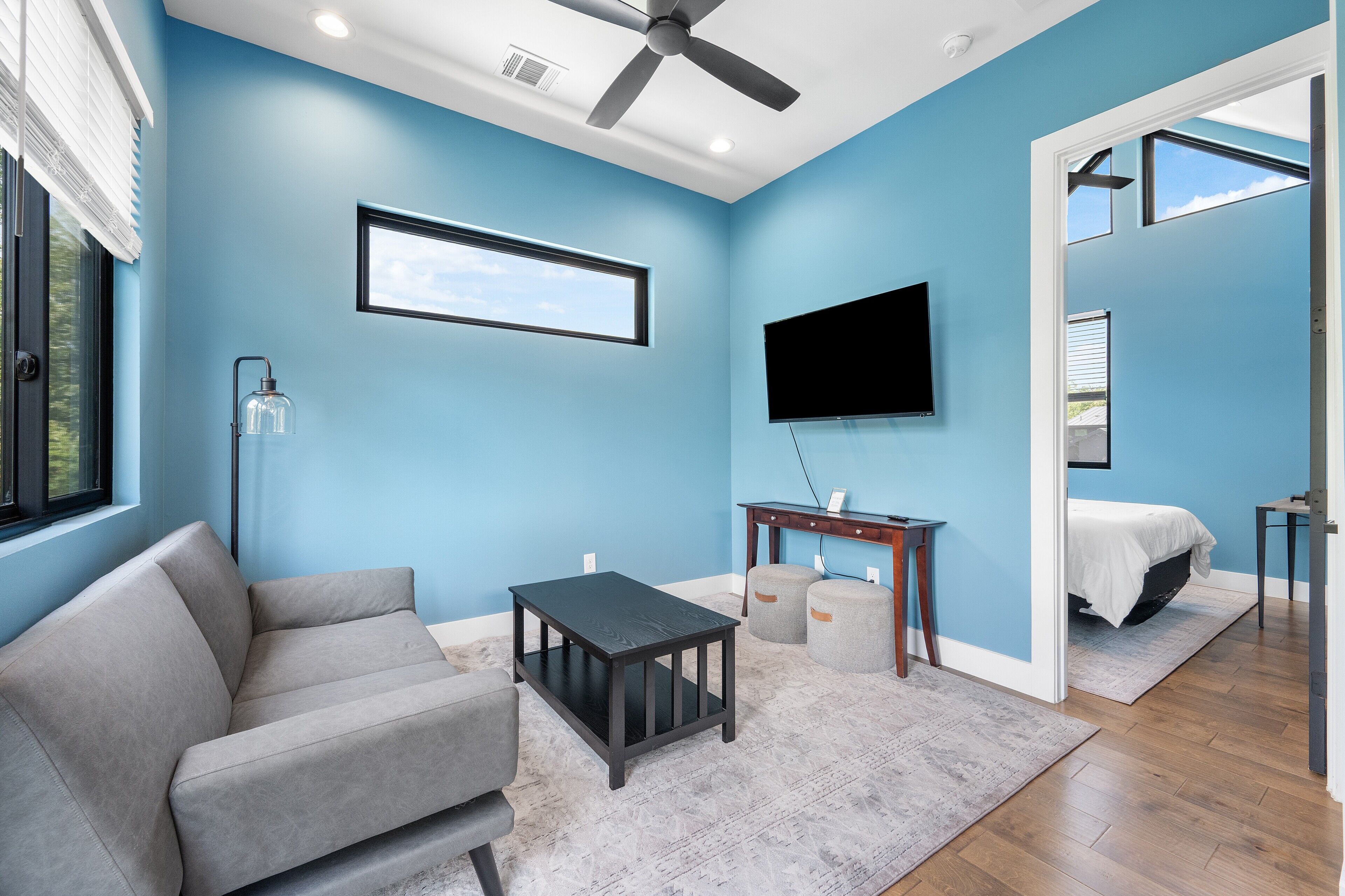 A modern living room with a grey sofa, a small table, a TV mounted on the wall, and a ceiling fan.