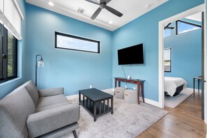 Un salon moderne avec un canapé gris, une petite table, un téléviseur fixé au mur et un ventilateur de plafond.
