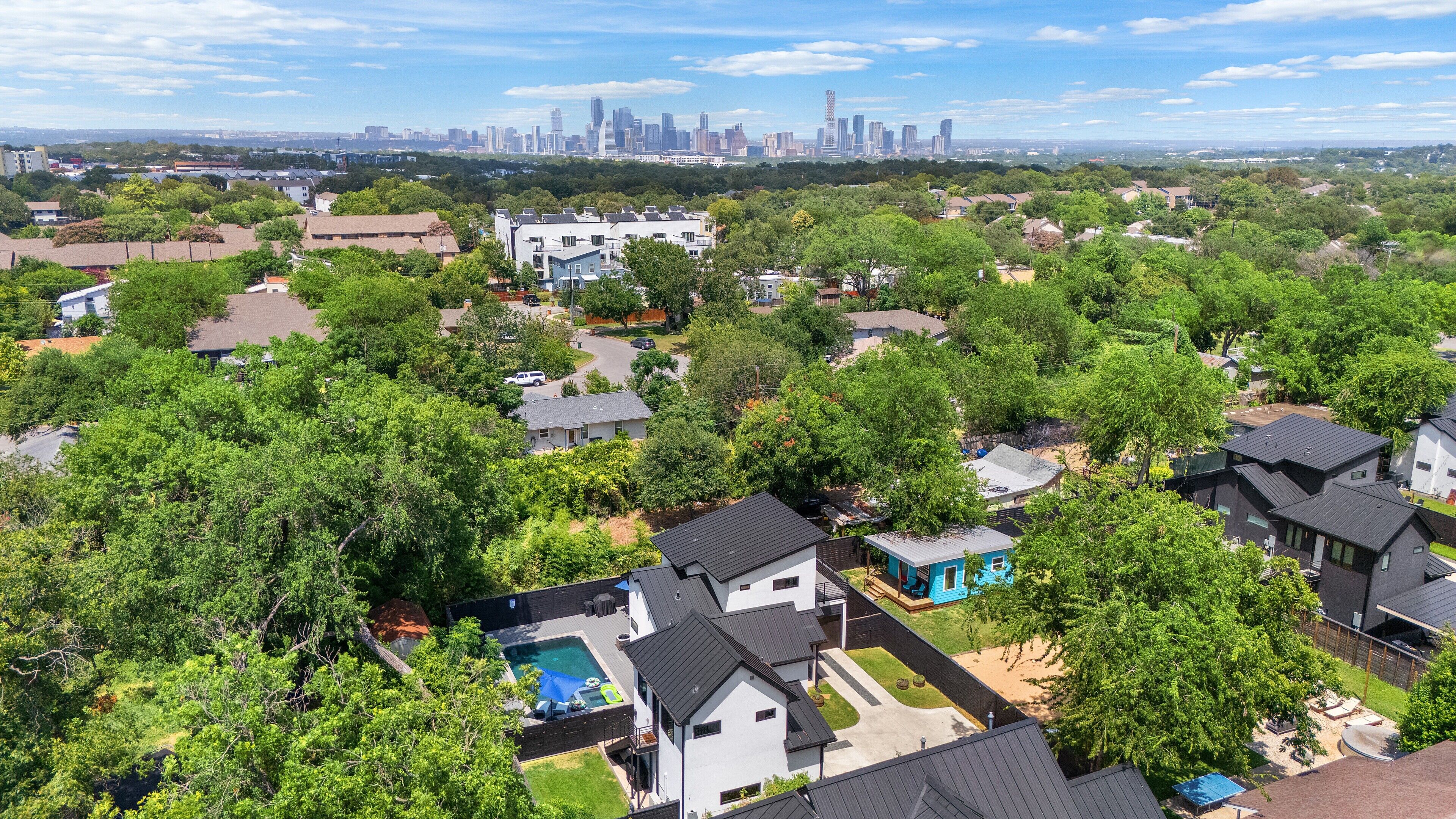 A residential area with houses, a swimming pool, and a city skyline in the background.