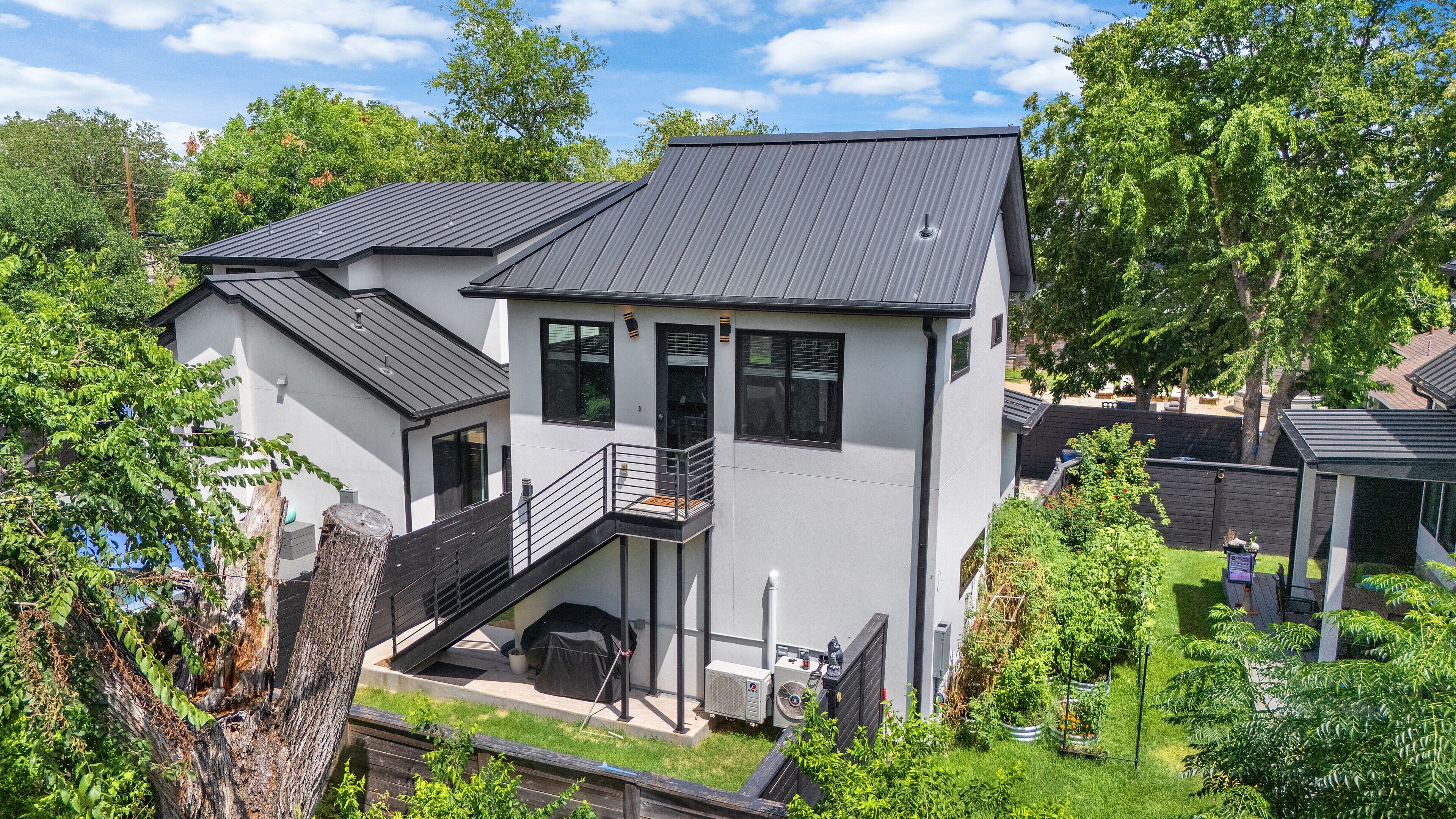 Une maison moderne à deux étages, dotée d’un balcon, d’un espace extérieur aménagé et couvert, et d’un jardin bien entretenu.
