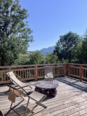 Une terrasse en bois avec deux chaises longues et une table ronde, offrant une vue sur un paysage montagneux.
