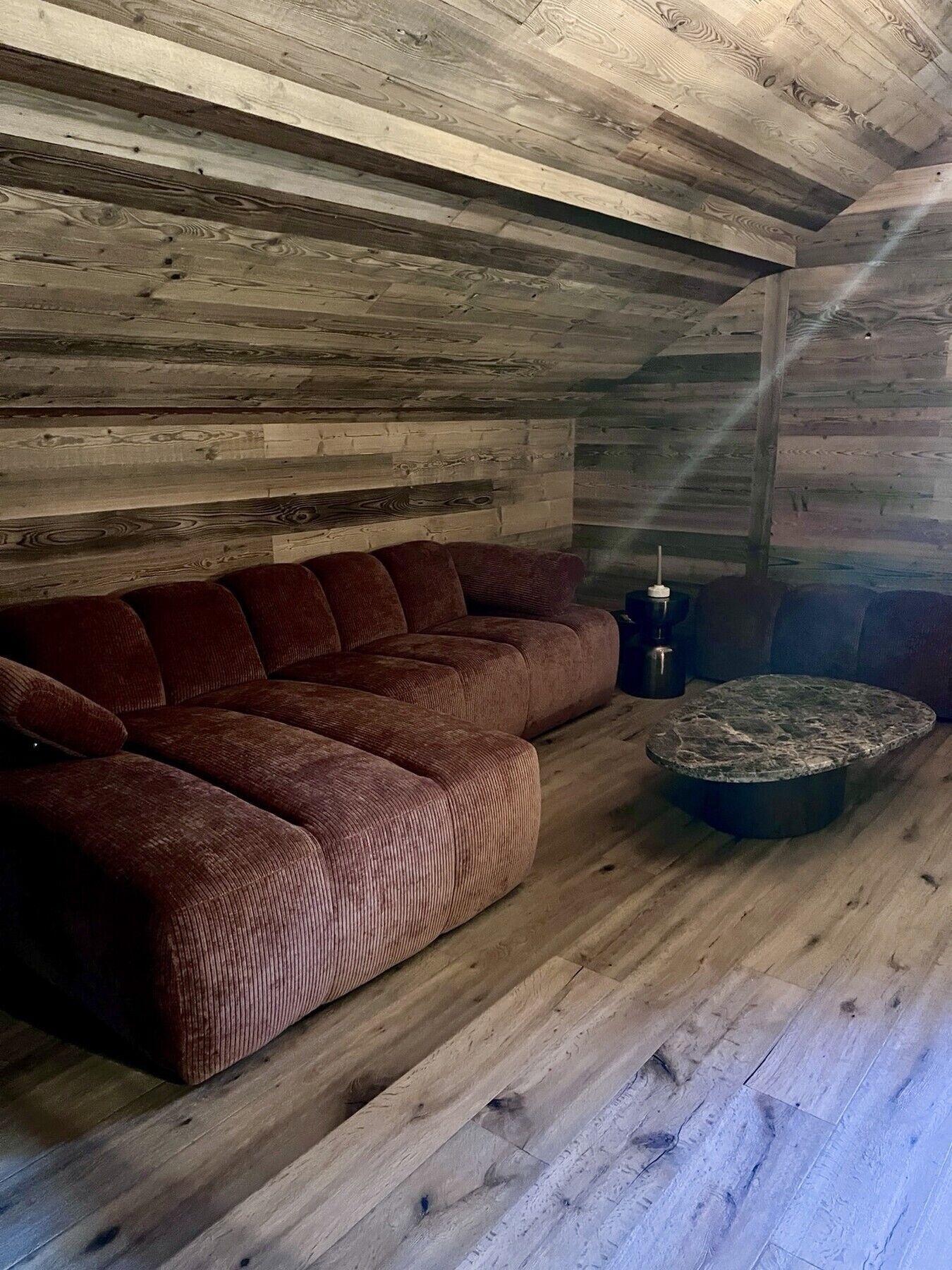 A cozy room with a wooden ceiling, a brown sofa, and a stone coffee table.