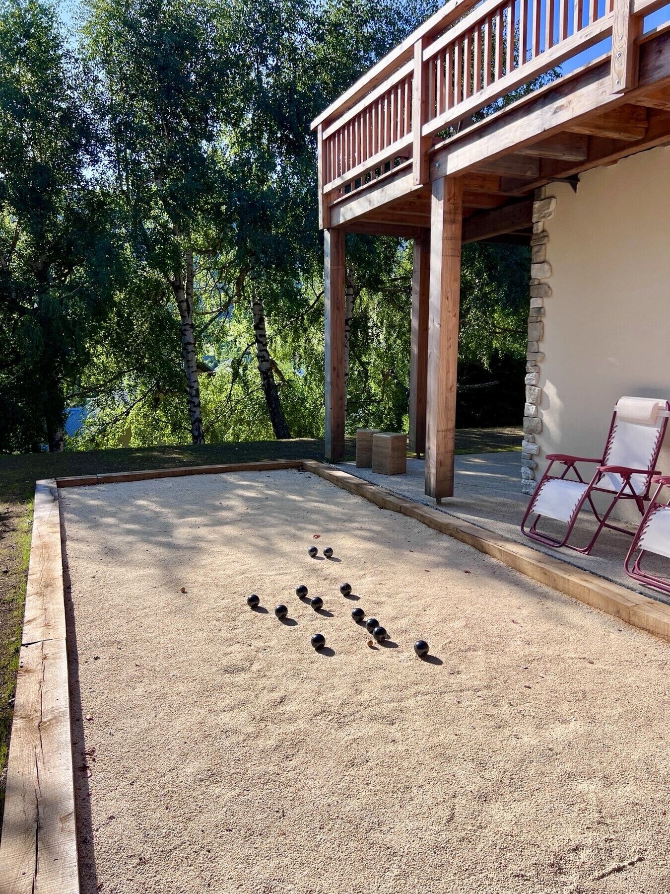 Un patio con una pérgola de madera, un muro de piedra y una zona de estar con sillas.
