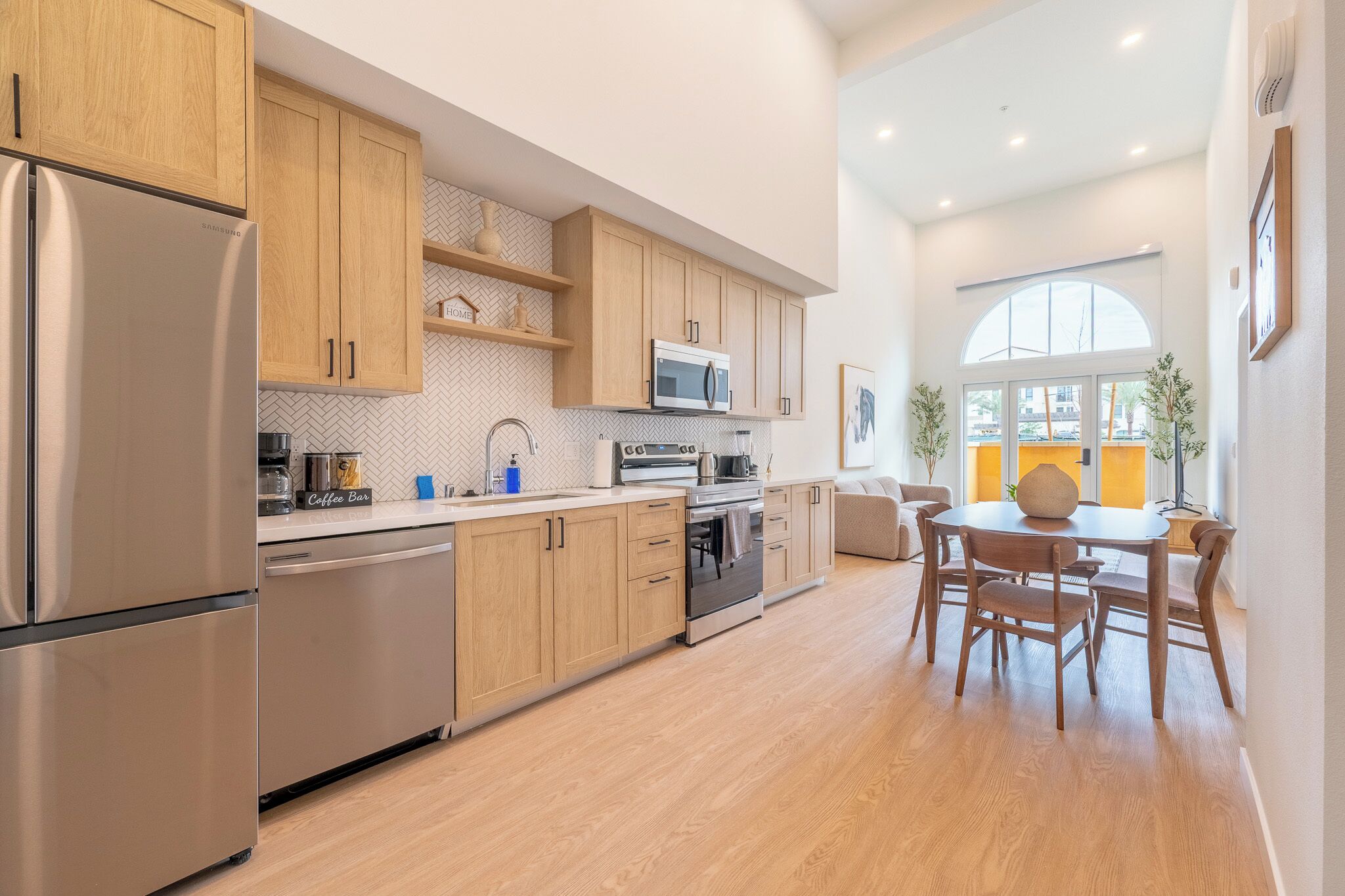 A modern kitchen with wooden cabinets, stainless steel appliances, and a dining area with a round table and chairs.
