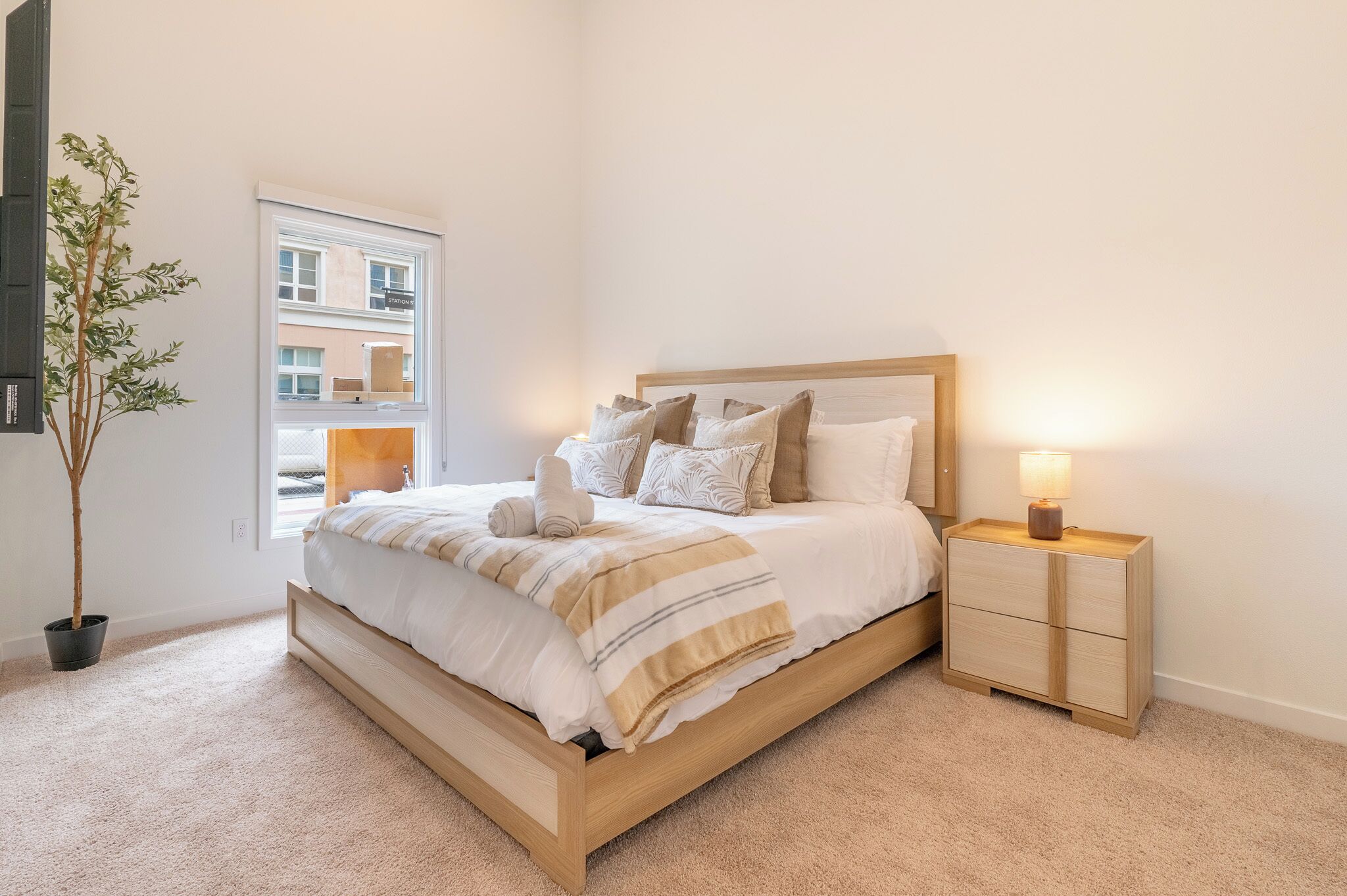 Ein Schlafzimmer mit Bett, Nachttisch, Lampe und einer Topfpflanze.