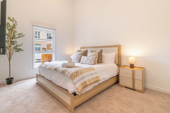 A bedroom with a bed, bedside table, lamp, and a potted plant.