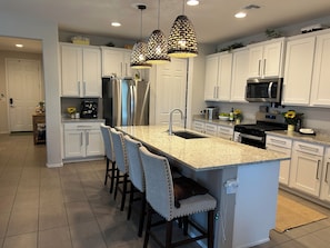 A modern kitchen with white cabinets, a granite countertop, stainless steel appliances, and pendant lighting.