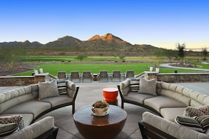 A patio with a sofa and chairs facing a golf course and mountains.