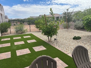 A backyard with artificial grass, a patio area, and a gravel section.