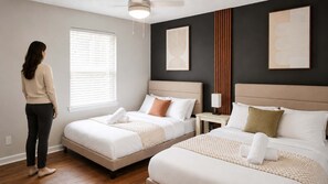 A hotel room with two beds, a window with blinds, a bedside table with a lamp, and artwork on the walls. - Urban Oasis | Stylish 2BR Near Med District w/ Pool & Free Parking (Dallas)