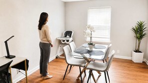 A room with a dining table, chairs, a potted plant, and a standing desk with a chair. - Urban Oasis | Stylish 2BR Near Med District w/ Pool & Free Parking (Dallas)