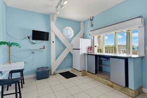 A kitchen with a large window, a flat-screen TV mounted on the wall, and a small dining area with a table and chairs. - Oceanfront pool, hot tub and game room (North Topsail Beach)