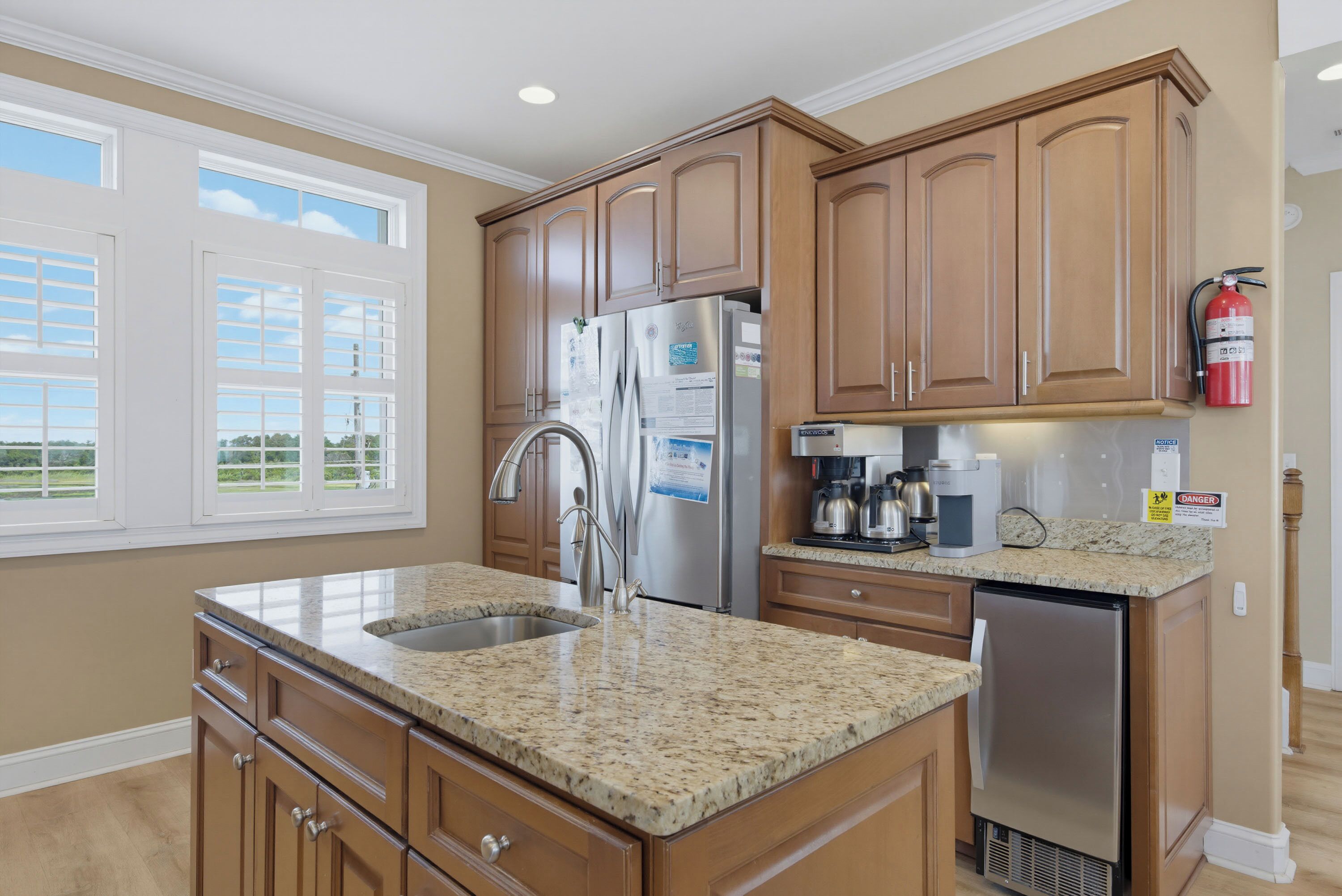 A kitchen with wooden cabinets, stainless steel appliances, a granite countertop, and a window with blinds.