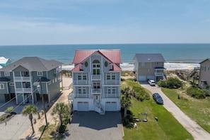 A multi-story residential building with a red roof, located near a beach with the ocean in the background. - Oceanfront pool, hot tub and game room (North Topsail Beach)
