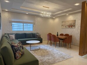 A modern living room with a sectional sofa, a round coffee table, and a dining area with a wooden table and chairs. - Stunning luxury apartment in a secure residence, close to everything (Agadir)
