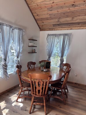A dining area with a wooden table and chairs, striped curtains, and a view through the window. - 3 bedroom house in quiet Warsaw neighborhood sitting on Lake of the Ozarks! (Warsaw)