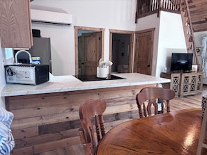 A kitchen with a microwave, sink, and wooden cabinets. There is a dining table with chairs and a television on a cabinet.