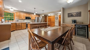 A spacious kitchen with wooden cabinets, a central island, and a dining area with chairs. - Lakefront on Winnipesaukee - Private Dock, Beach & Firepit - Sleeps 10 (Laconia)