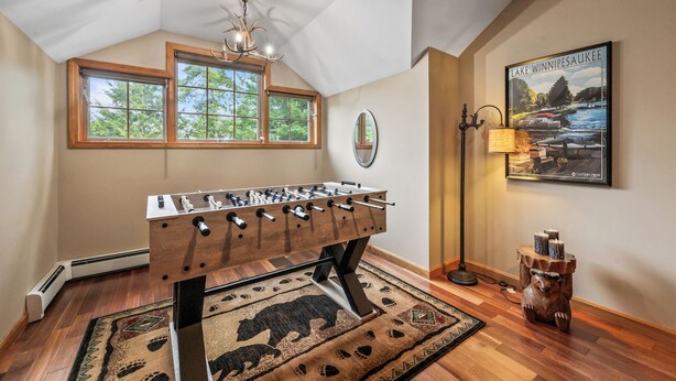 A room with a foosball table, a chandelier, a poster of Lake Winnipeg, and a bear statue. - Lakefront on Winnipesaukee - Private Dock, Beach & Firepit - Sleeps 10 (Laconia)