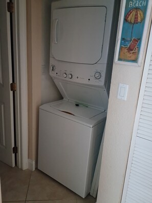 A compact laundry room with a washing machine and dryer, a door, and a wall-mounted poster.