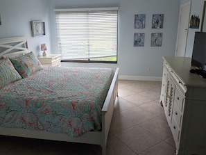 A bedroom with a bed, a dresser, a window with blinds, and wall art.