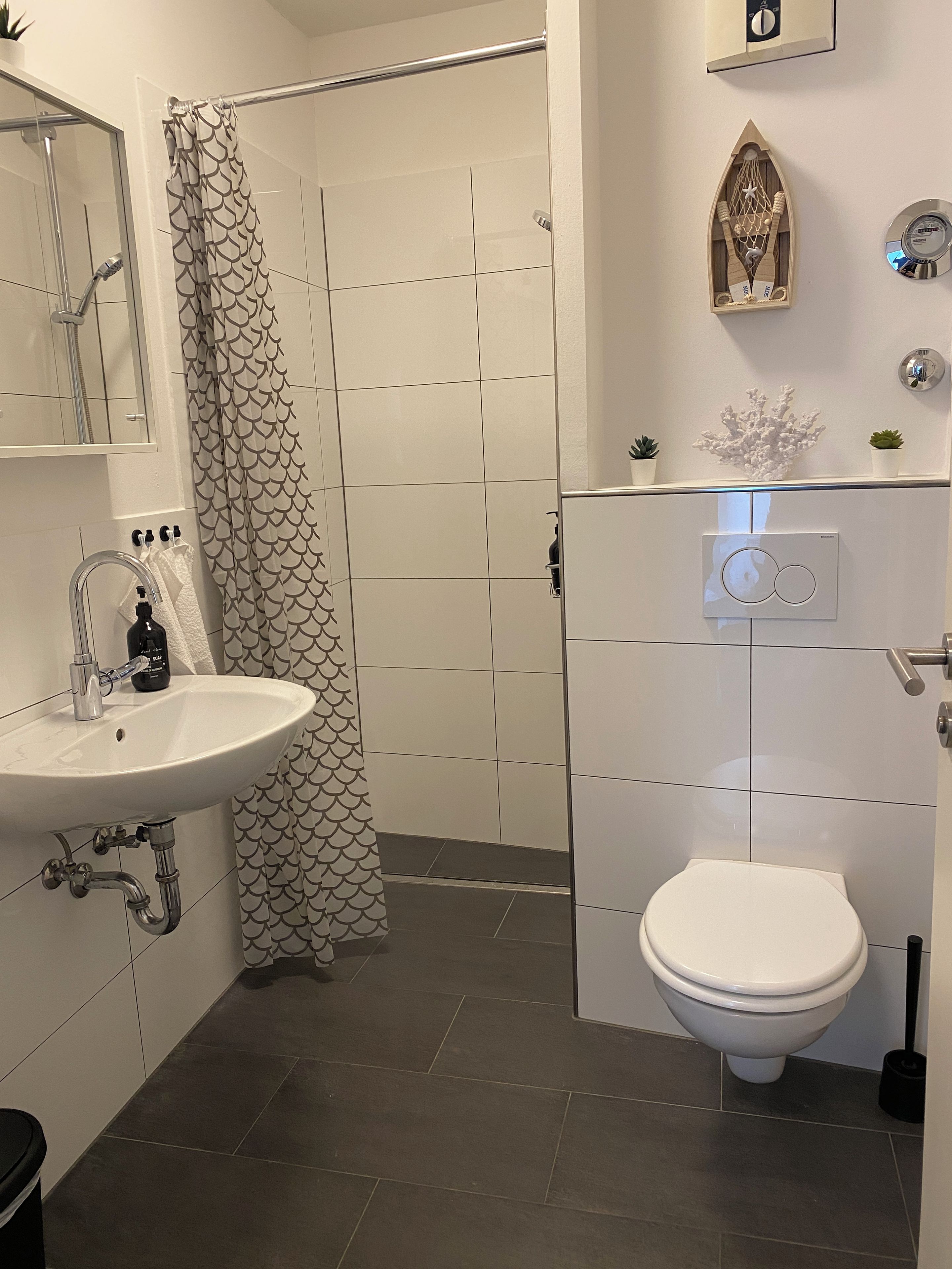Ein modernes Badezimmer mit Waschbecken, Toilette und Duschbereich, alles in Weiß.