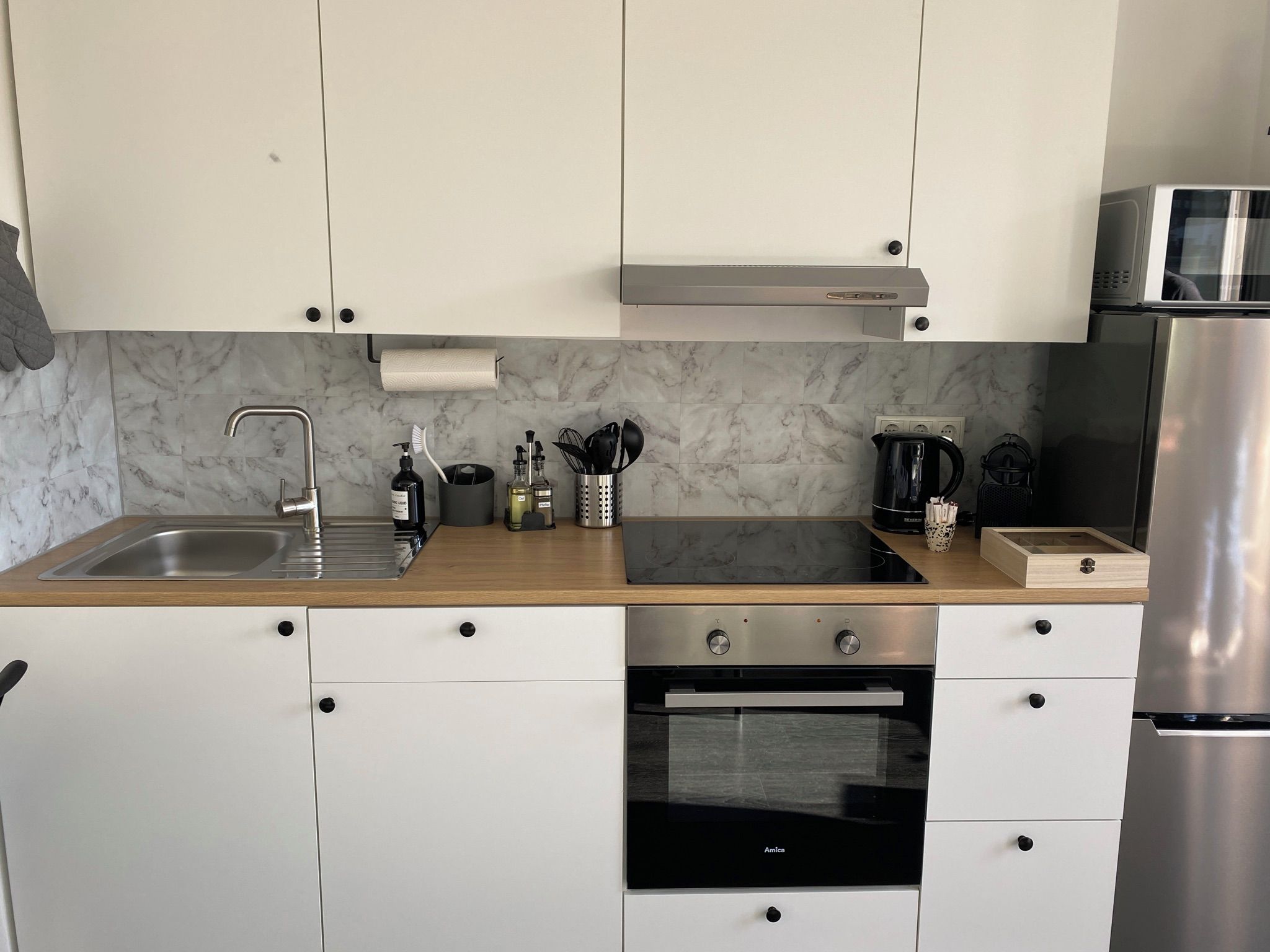 Eine moderne Küche mit weißen Schränken, einer Edelstahl-Spüle, einem eingebauten Backofen und einer Mikrowelle.