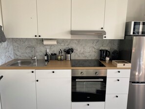 Eine moderne Küche mit weißen Schränken, einer Edelstahl-Spüle, einem eingebauten Backofen und einer Mikrowelle.