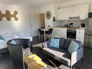 Ein modernes Hotelzimmer mit Bett, einer Couch, einem Esstisch und einer Küchenzeile.