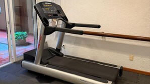 Un tapis roulant in una stanza con pavimento piastrellato, una porta vetrata che dà all'esterno e un pannello di controllo montato a parete.