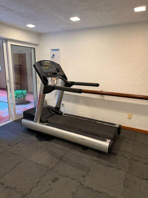 Ein Laufband in einem Raum mit Fliesenboden, einer Glastür, die nach draußen führt, und einer an der Wand befestigten Steuerung.