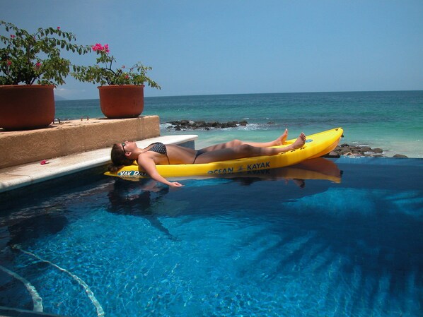 A person lying on a yellow kayak in a pool with clear blue water and a view of the ocean. - Private beachfront villa w/ private pool and chef (Puerto Vallarta)
