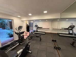 Ein Fitnessstudio mit Trainingsgeräten, darunter Laufbänder, ein Ergometer und Kurzhanteln.