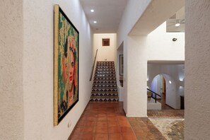 Ein Korridor mit Fliesenboden, einer Treppe mit gemusterten Kacheln und einem großen Gemälde an der Wand.