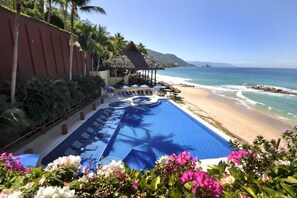 Ein Pool in einem Resort mit Liegestühlen, einem Strand und einem Berg im Hintergrund.