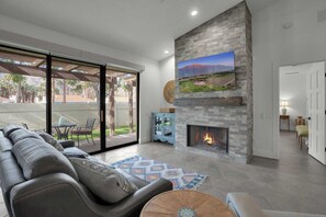 Ein modernes Wohnzimmer mit Kamin, großem Wand-Fernseher und gemütlicher Sitzecke inklusive Sofa und Couchtisch.